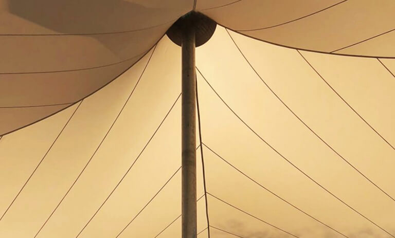 Central vertical pole supporting a beige tent canopy with radiating tension lines against a sunlit sky.