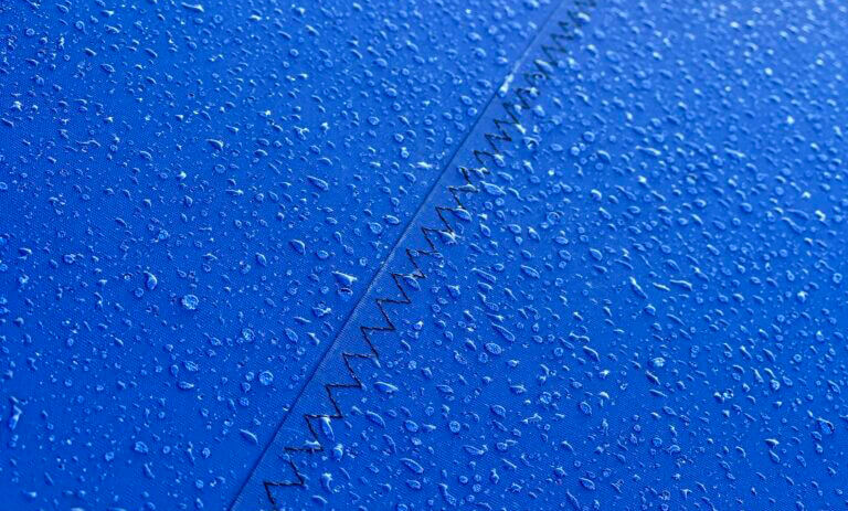 Close-up of blue fabric with raindrops and a stitched seam forming a diagonal line.